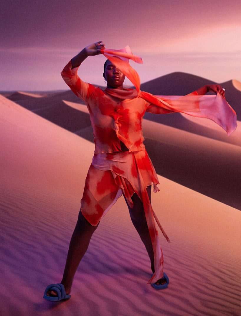 Woman in an orange tie-dye outfit poses in the desert with a scarf. Dramatic desert landscape. Atmospheric lighting. Fashion.
