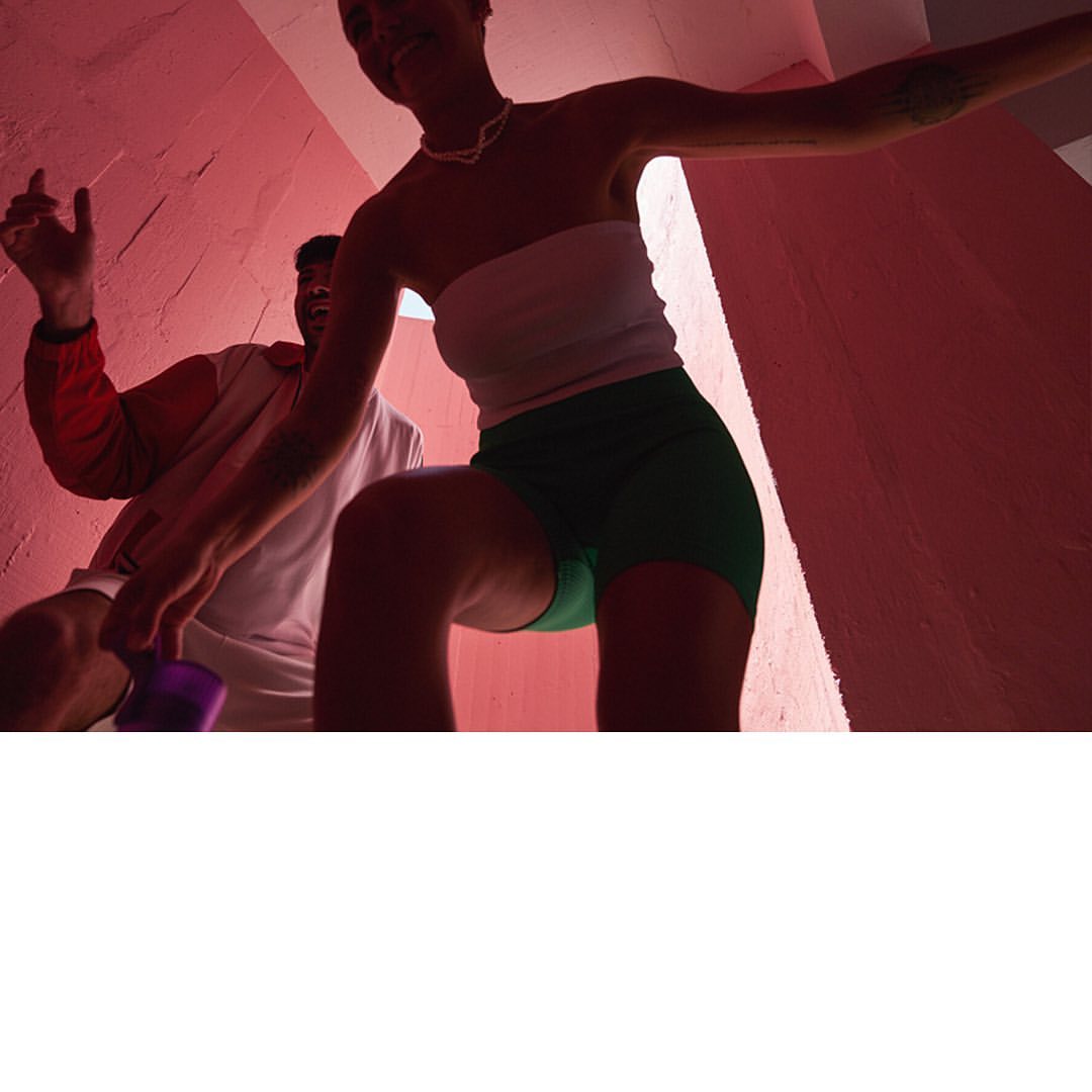 Two people, an adult woman and an adult man, in a brightly lit room, with pink walls and a low-angle view, with the woman in the foreground.