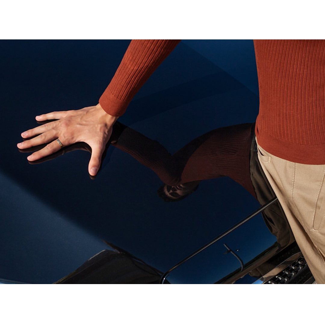 Close-up of a man's hand touching a dark blue glossy surface, with a reflection of the person's torso and head visible in the glossy finish.