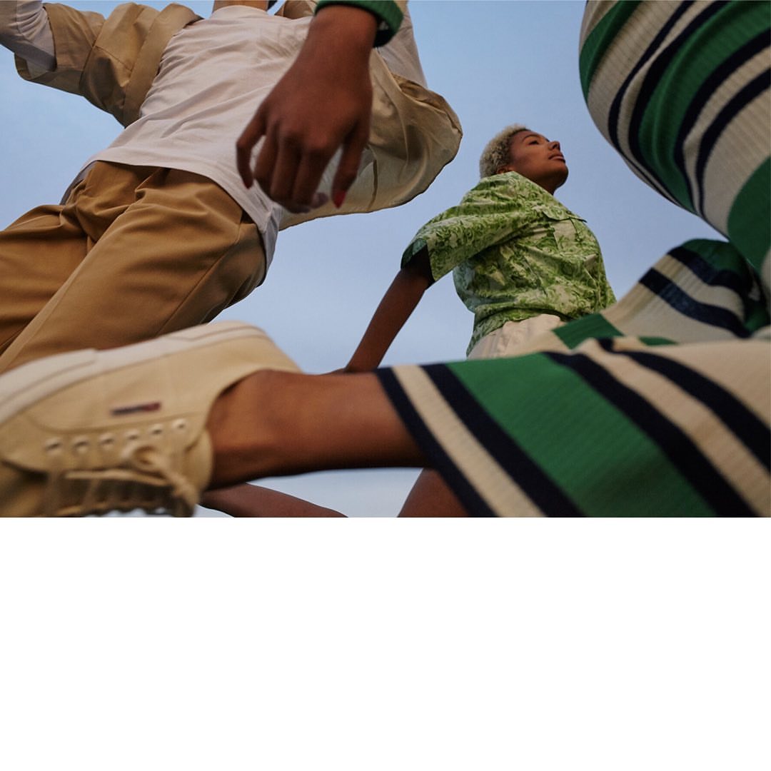 Three young adult fashion models wearing casual clothing in an outdoor setting with a low-angle perspective and blue sky background.