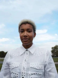 Portrait of a black woman with short blonde hair wearing a white western shirt against an overcast sky and park background