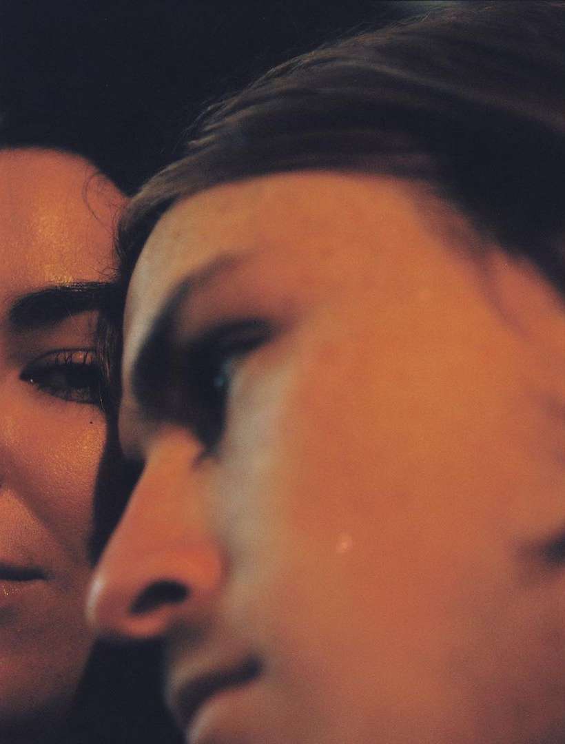 Close-up of two individuals, one adult male with a tear on his face, captured in shallow focus with warm lighting against a dark backdrop.