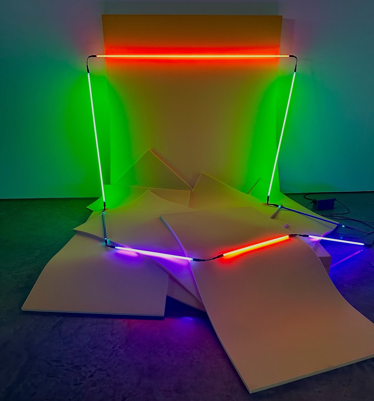 Abstract installation art featuring vibrant neon lights arranged in geometric shapes against a backdrop of yellow panels and flooring.