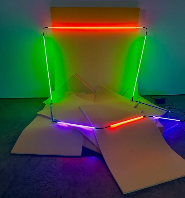 Abstract installation art featuring vibrant neon lights arranged in geometric shapes against a backdrop of yellow panels and flooring.