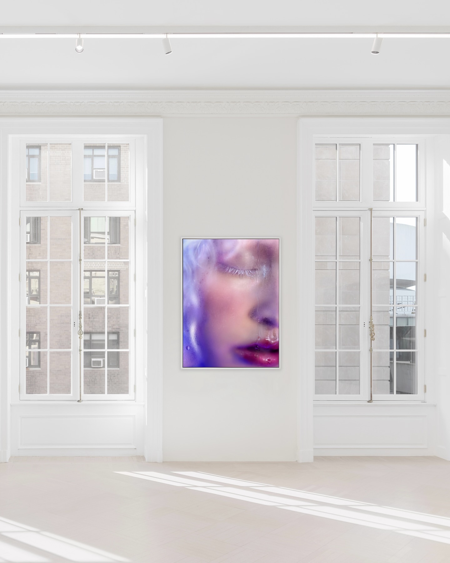 Abstract digital art on a wall featuring a close-up of a woman's face with dreamy lighting and pastel color grading, inside a modern art gallery.