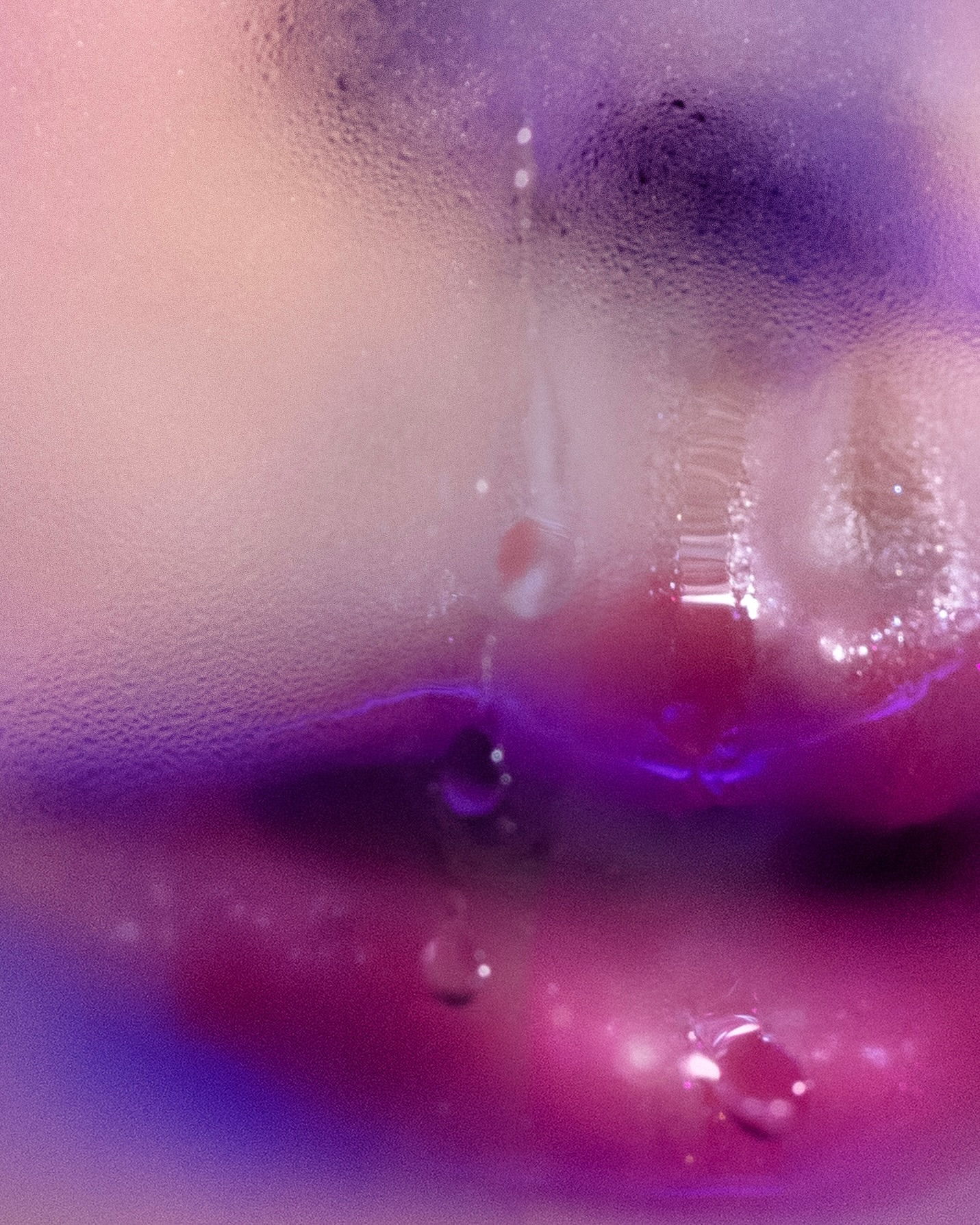 Close-up of a beverage glass showing condensation and water droplets, in a gradient of purple, pink, and peach hues.