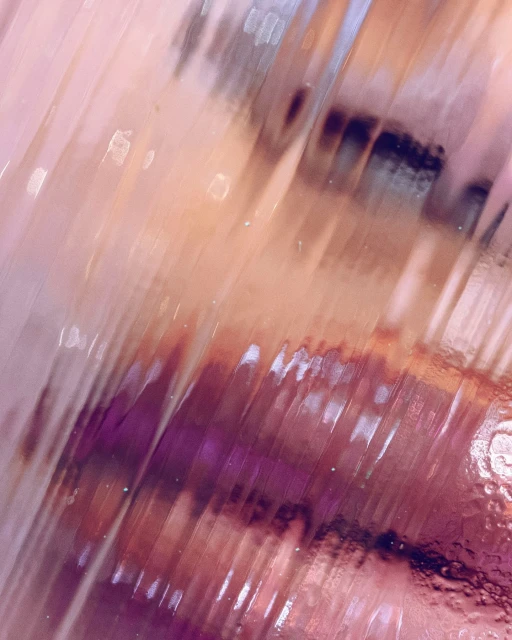 Abstract close-up of refracted light creating blurred, striped patterns of pink, purple, and brown, resulting in an indistinct, textured effect.
