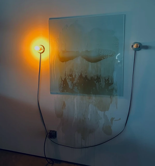 Abstract art piece featuring a textured blue and brown panel lit by two sconce lights against a neutral wall in a minimalist setting.