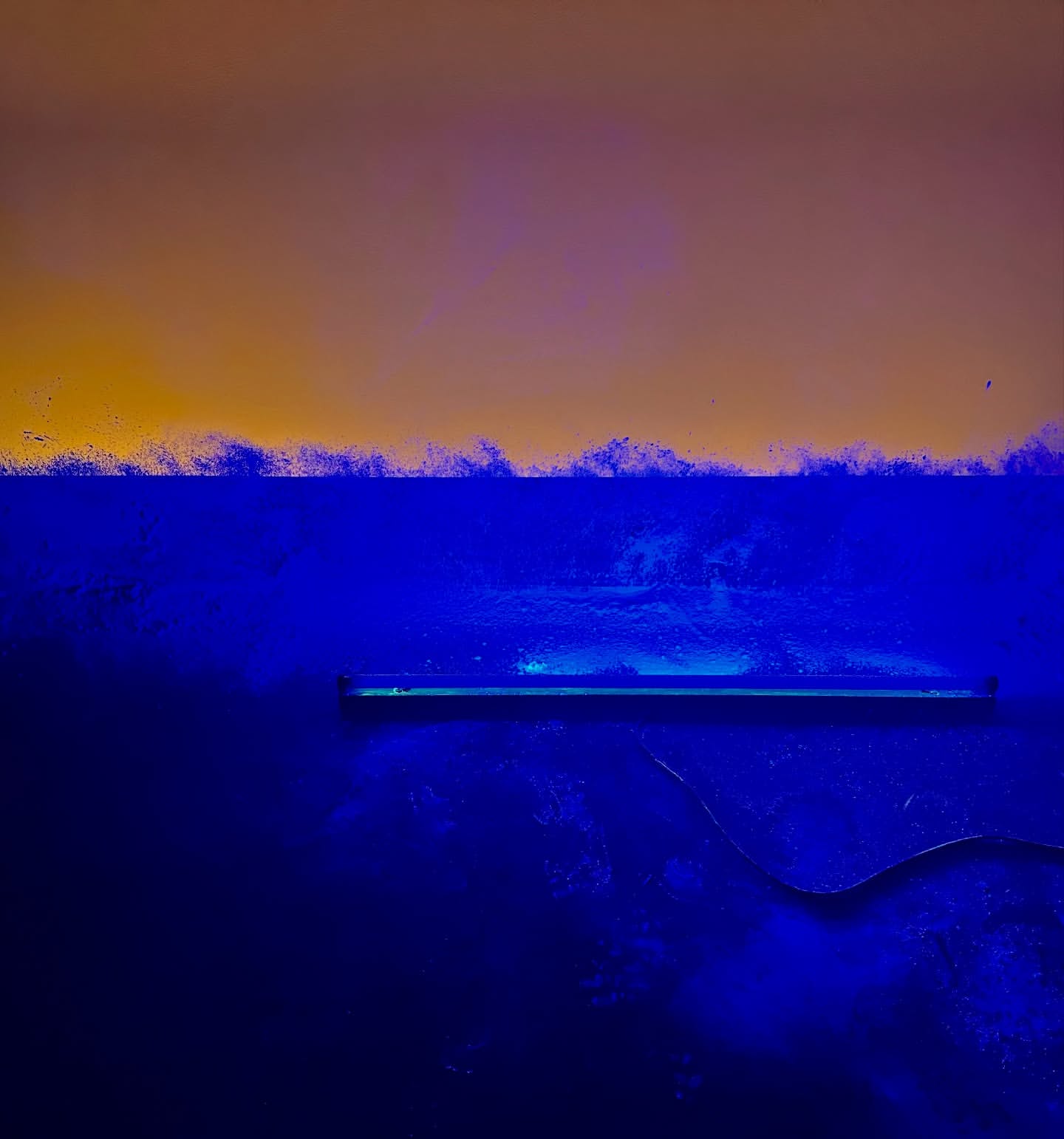 Abstract art image of an illuminated blue wall, with light reflecting off the surface against a golden-orange backdrop. Moody lighting.