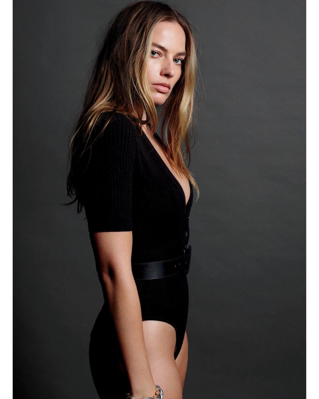 Portrait of Margot Robbie wearing a black bodysuit against a plain dark grey studio backdrop