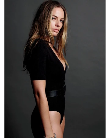 Portrait of Margot Robbie wearing a black bodysuit against a plain dark grey studio backdrop