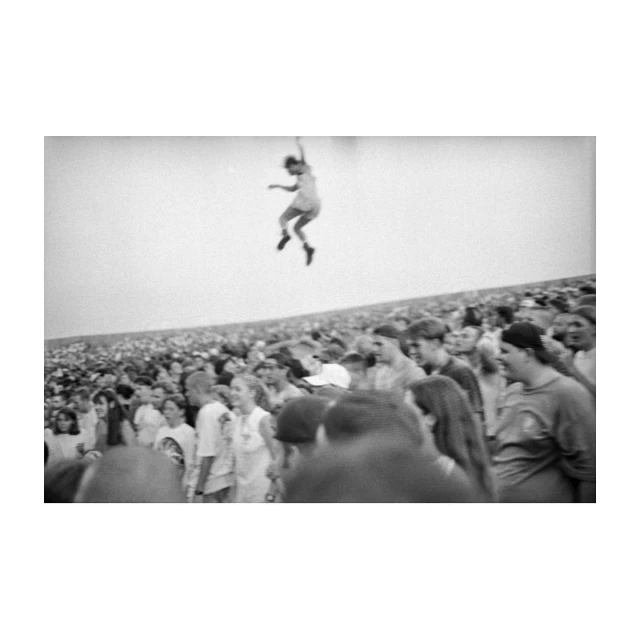 Black and white crowd scene featuring a person jumping in the air. A large group of onlookers is captured in this outdoor setting.