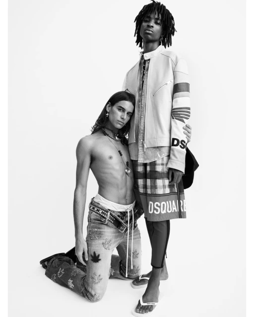 Two male fashion models pose against a white backdrop. One kneels in jeans and the other stands in shorts with the Dsquared2 logo.