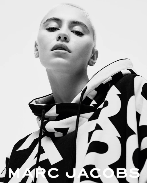 Close-up shot of a young adult female with a shaved head, wearing a black and white patterned hoodie with the Marc Jacobs logo.