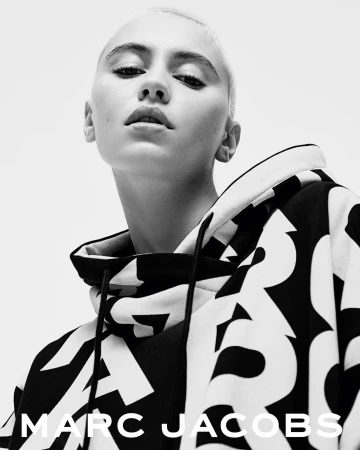 Close-up shot of a young adult female with a shaved head, wearing a black and white patterned hoodie with the Marc Jacobs logo.