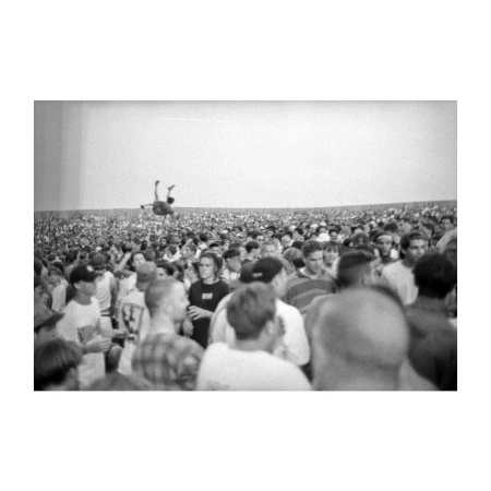 A crowd of people watching a person performing a stunt in the air, captured in black and white with a clear division of space.