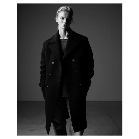 Model wearing a dark double breasted wool coat in a black and white studio portrait photographed by Mario Sorrenti.