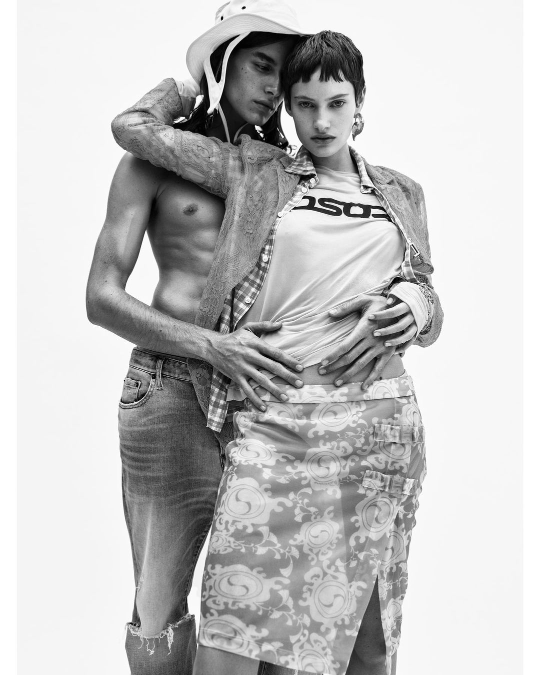 A couple poses in an indoor studio in front of a white backdrop. The man has a cowboy hat, and the woman has a graphic tee.