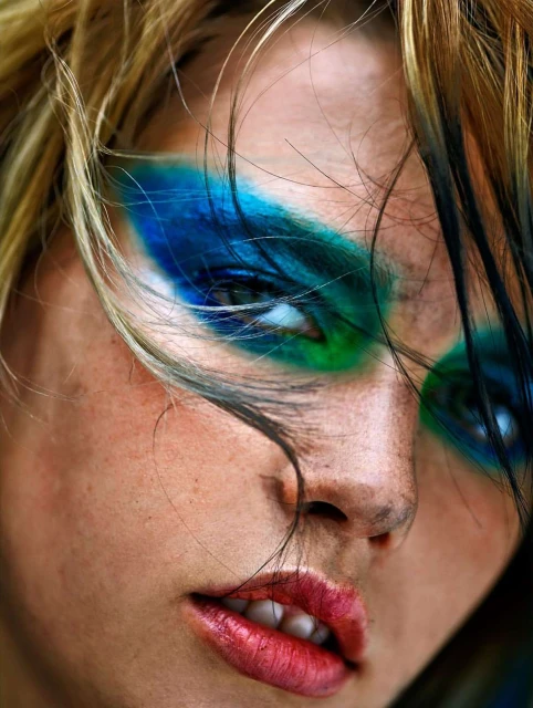 Close-up of a woman's face with striking blue and green eye makeup and red lips, capturing a bold and artistic beauty statement.
