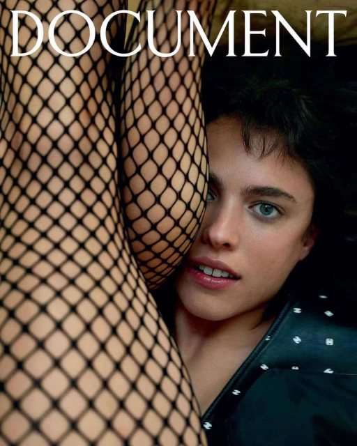 Close-up fashion portrait of a young woman with blue eyes and dark hair next to legs in black fishnet tights with a tan background.