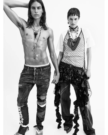 Black-and-white fashion shot of a shirtless man with long hair and a woman with short hair holding hands in front of a white background.