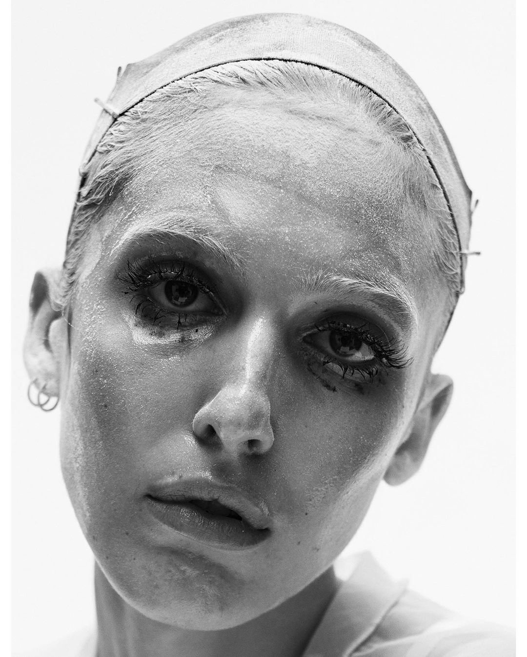 Monochrome portrait of an adult woman with dramatic eye makeup and a metallic head covering in a brightly lit photo studio.