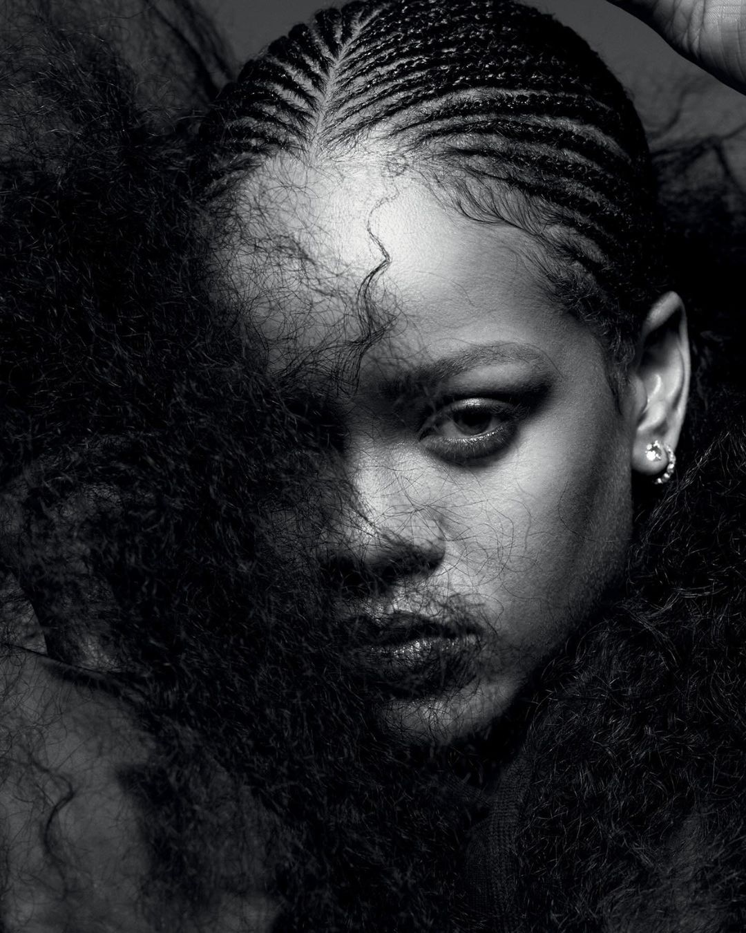 Striking black-and-white portrait of a woman with braided hair, partially obscured by dark, voluminous curls, focusing on her intense gaze.