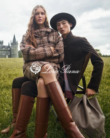 Two models, an adult woman and an adult man, are posed outdoors in riding boots, skirts, jackets with a castle in the background.