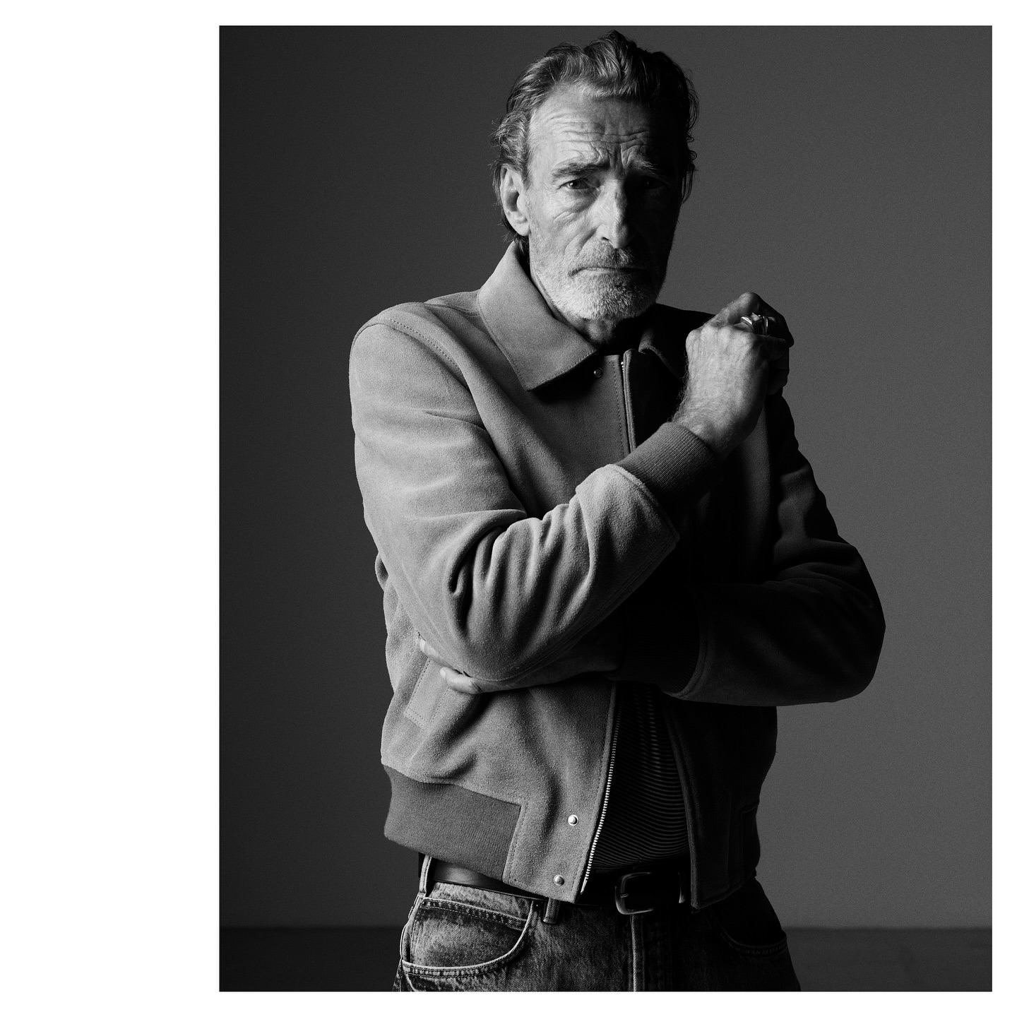 Black and white portrait of an older man with grey hair wearing a zipped jacket against a plain background
