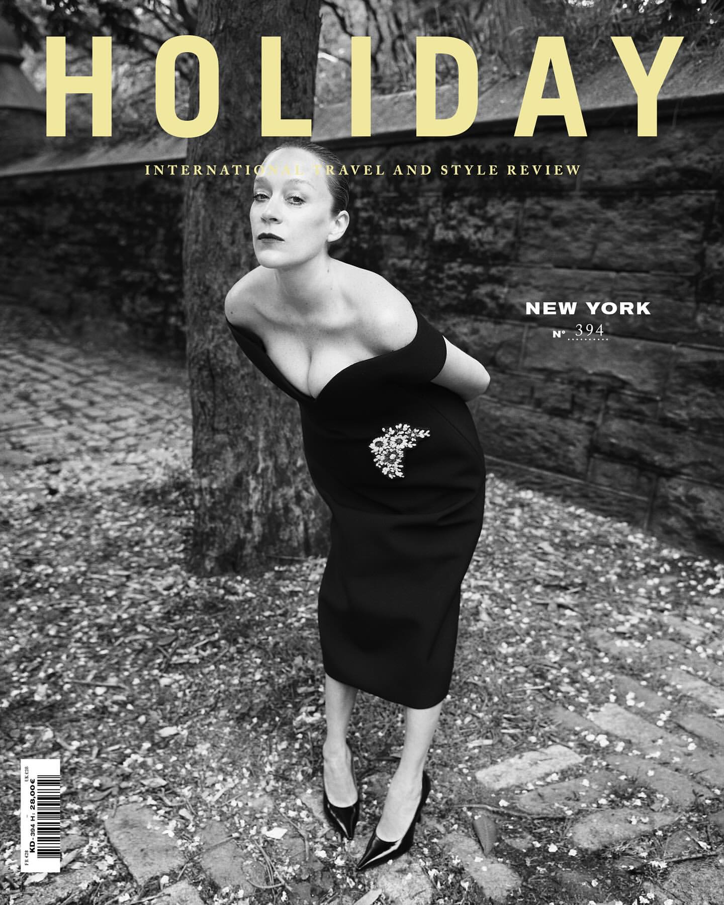 Black and white magazine cover featuring a woman in a black dress, posing against a backdrop of stone and foliage with ‘HOLIDAY’ in yellow text.