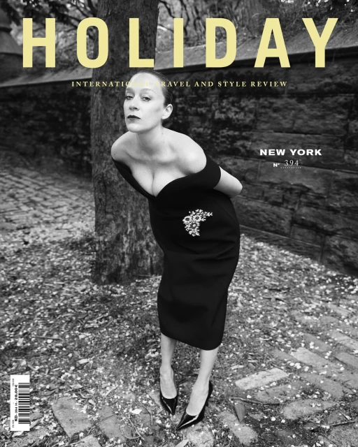 Black and white magazine cover featuring a woman in a black dress, posing against a backdrop of stone and foliage with ‘HOLIDAY’ in yellow text.