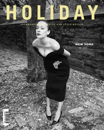 Black and white magazine cover featuring a woman in a black dress, posing against a backdrop of stone and foliage with ‘HOLIDAY’ in yellow text.