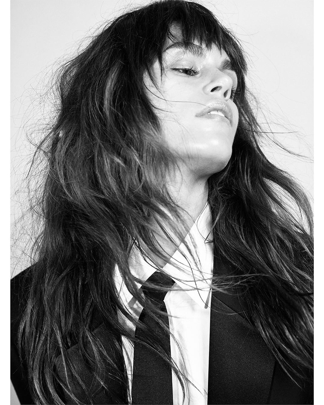 Monochrome portrait of a woman with dark hair and bangs wearing a white shirt and black suit jacket by Mario Sorrenti