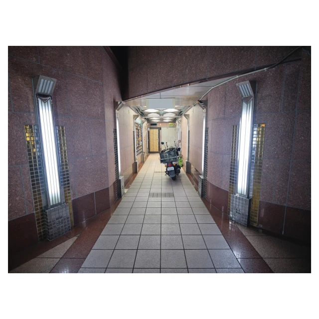 An indoor hallway with red and brown granite walls, tile flooring, fluorescent lighting, and a parked scooter at the far end.