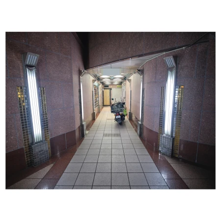 An indoor hallway with red and brown granite walls, tile flooring, fluorescent lighting, and a parked scooter at the far end.
