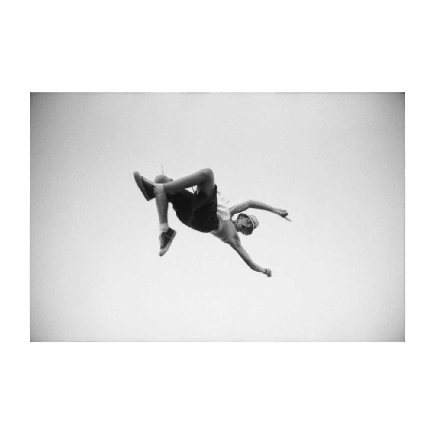 Monochrome portrait of a man performing a backflip against a bright sky, showcasing athleticism and acrobatic skill in an outdoor setting.