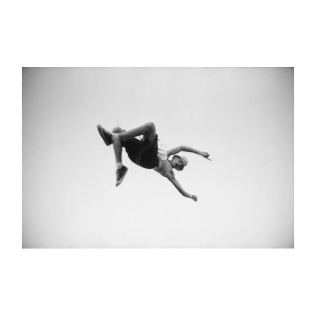 Monochrome portrait of a man performing a backflip against a bright sky, showcasing athleticism and acrobatic skill in an outdoor setting.
