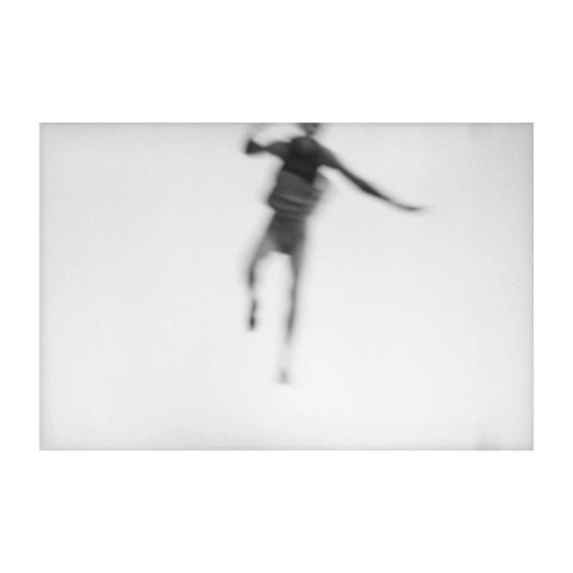 Blurry black and white photo of a man in mid-air with outstretched arms and legs, creating a sense of motion and energy.