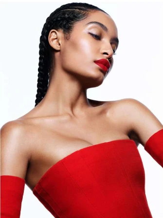 Close-up portrait of a woman with braided hair wearing a red strapless top against a white background