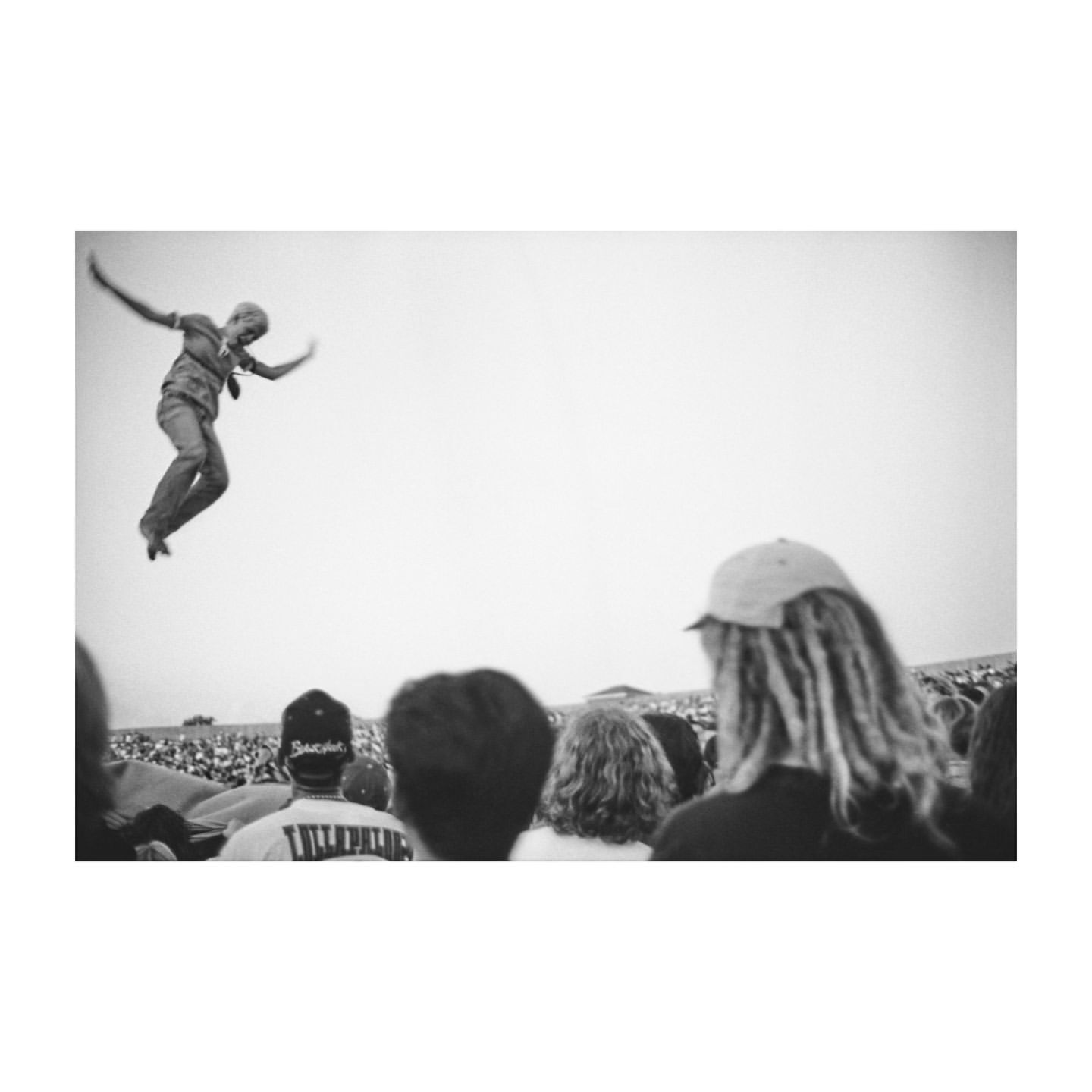 Black and white photograph by Mario Sorrenti of a person leaping mid air above a crowd of spectators.