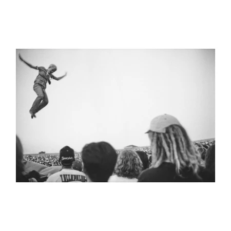 Black and white photograph by Mario Sorrenti of a person leaping mid air above a crowd of spectators.