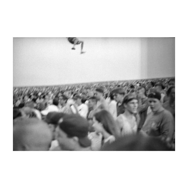 Black and white photograph of a large crowd of people with one person jumping high above them.