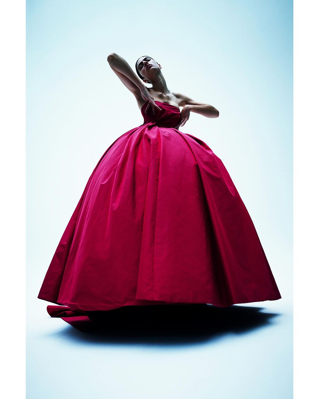 A striking fashion shot features a model in a full, bright pink ballgown, posed against a graduated blue background, under dramatic lighting.