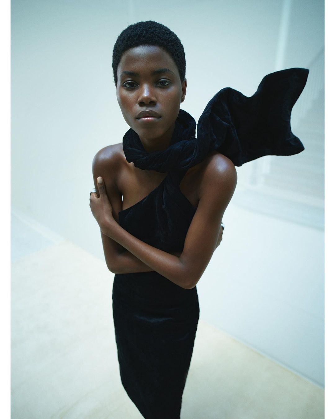 Striking studio shot of a Black female fashion model in a black dress with a large bow. She poses against a clean, light background.