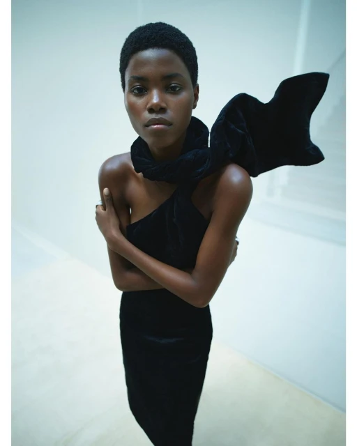 Striking studio shot of a Black female fashion model in a black dress with a large bow. She poses against a clean, light background.