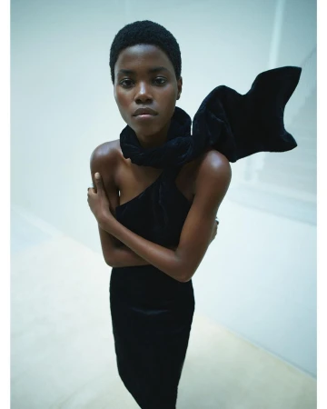 Striking studio shot of a Black female fashion model in a black dress with a large bow. She poses against a clean, light background.