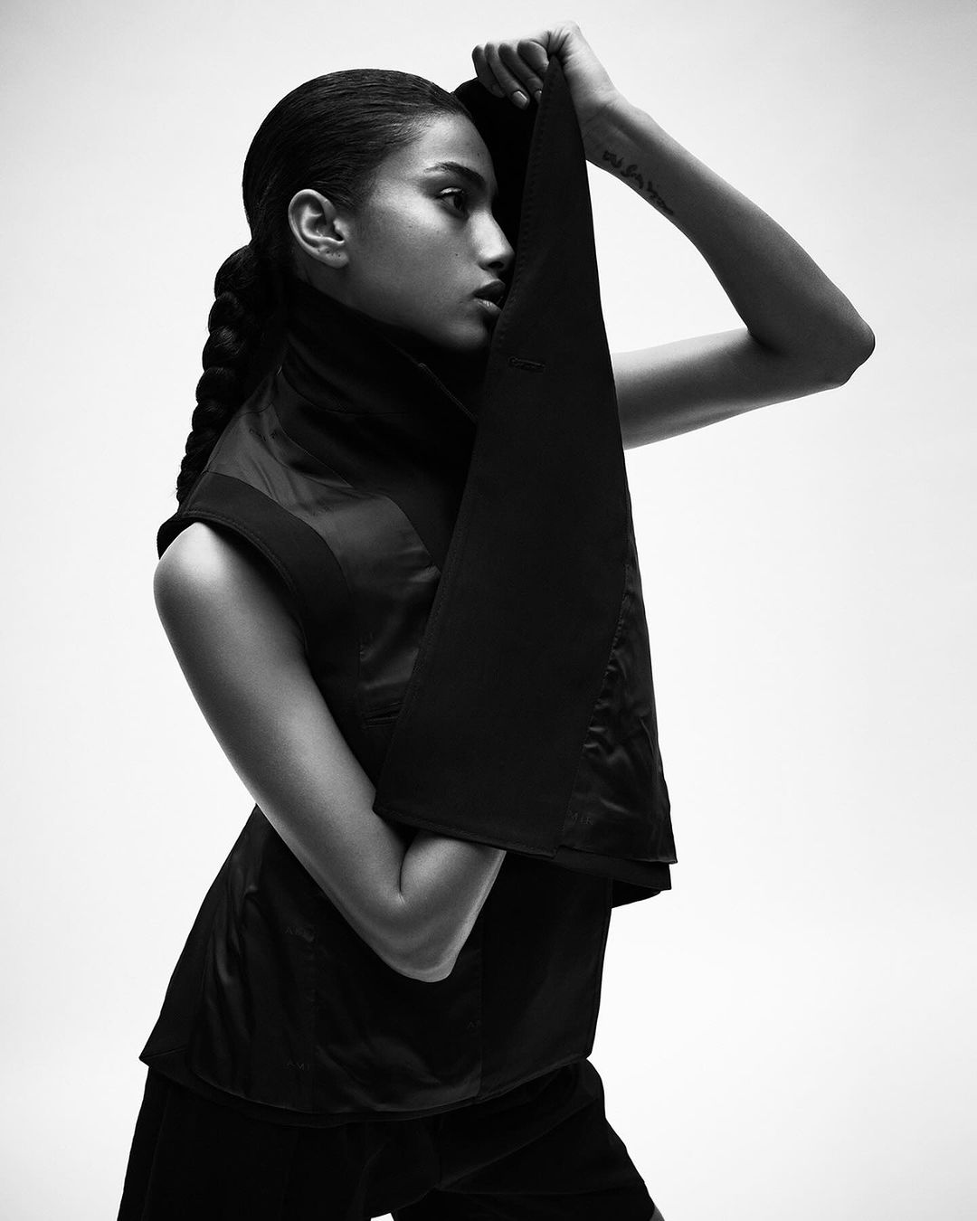 Black and white studio portrait of a Black woman in a sleeveless top, holding a piece of fabric above her head in a fashion pose.