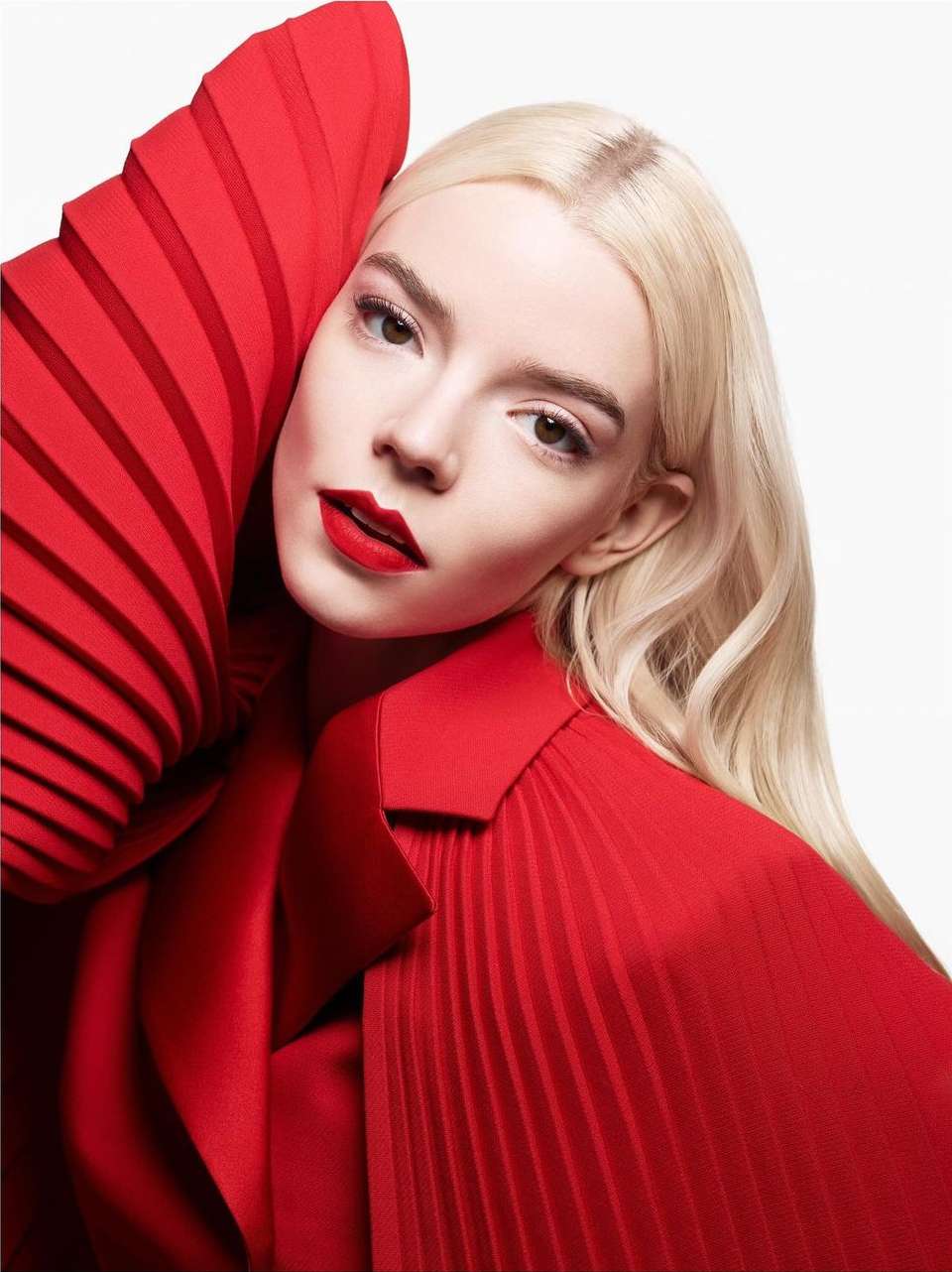 Close-up portrait of a platinum blonde adult female with red lipstick and red dress against a white background in a photo studio.
