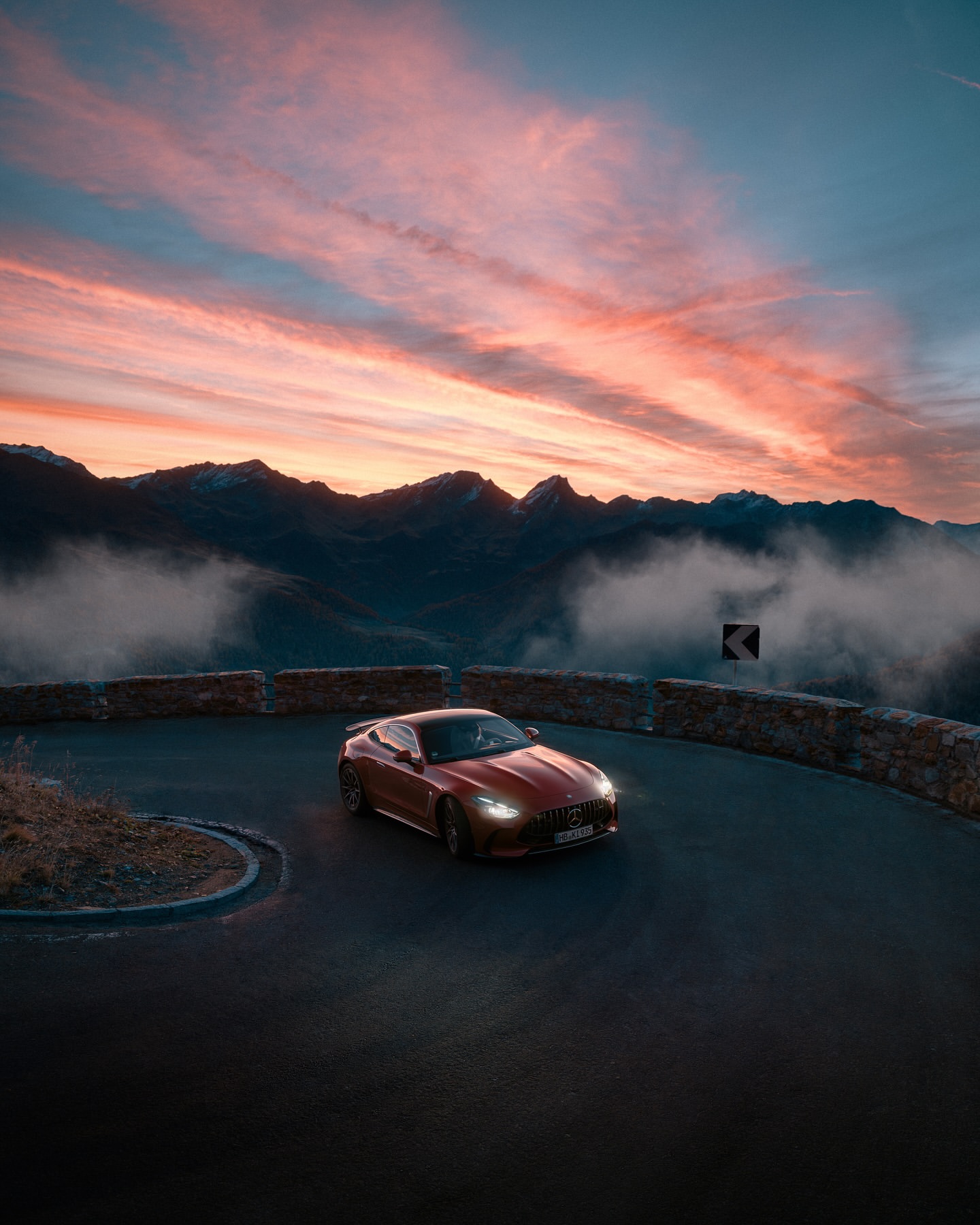 Red Mercedes-AMG driving on a winding mountain road at sunset, with dramatic sky and landscape views. Automotive photography.