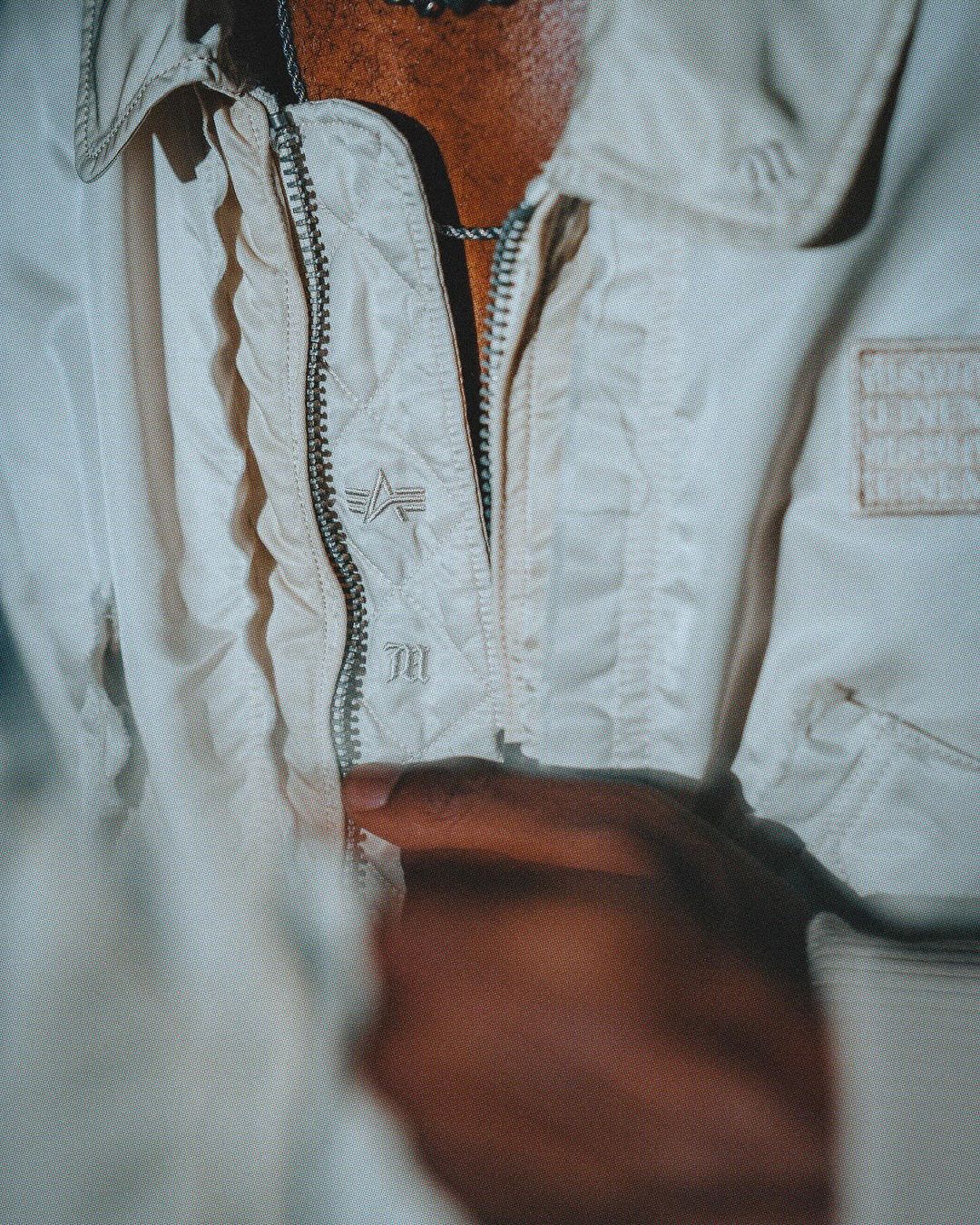 Close-up of a person in an off-white jacket with a zipper, showcasing a brand logo and the jacket's fabric texture and design details.